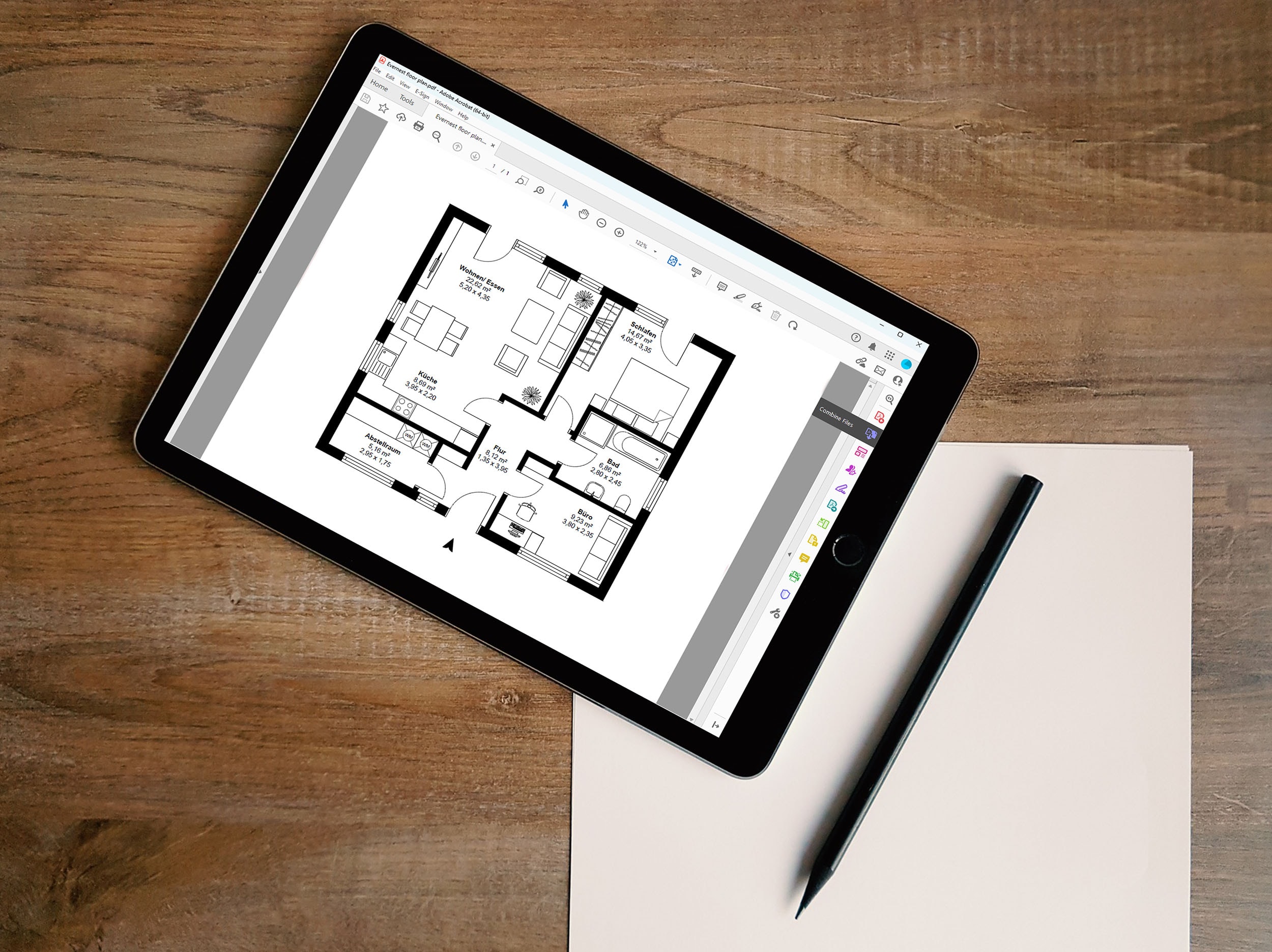 Ein auf einem Holztisch liegendes Tablet, dass den Grundriss einer 3-Zimmer Wohnung mit offener Küche und Abstellraum zeigt.