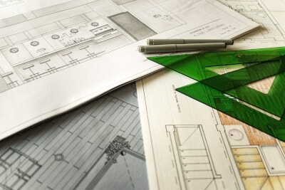 Detailed shot of several construction drawings stacked on top of each other with pens and triangular rulers