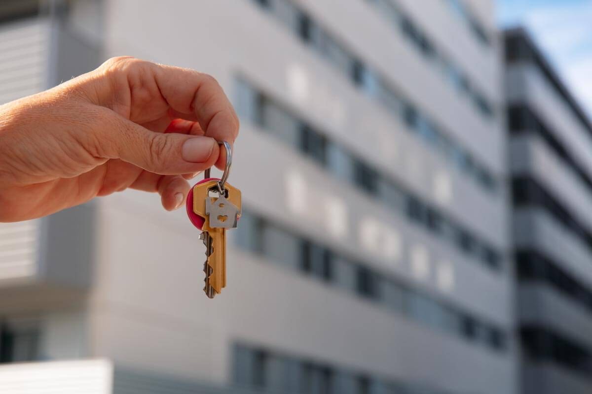 Hand holding a bunch of house keys against a blurred outdoor background; symbolic image of a property handover and rental agreement.