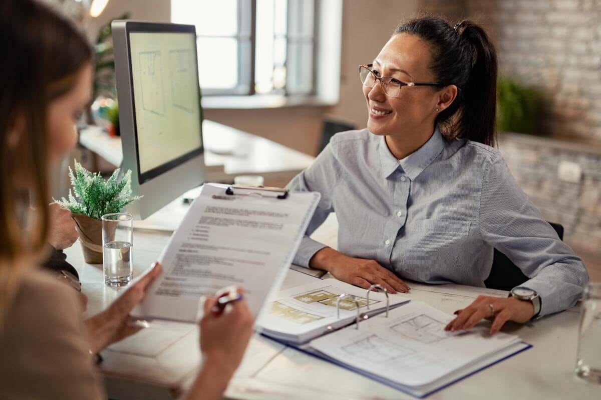A smiling female estate agent explains contract details to a couple at a table; symbolic image of advice on rental guarantees.