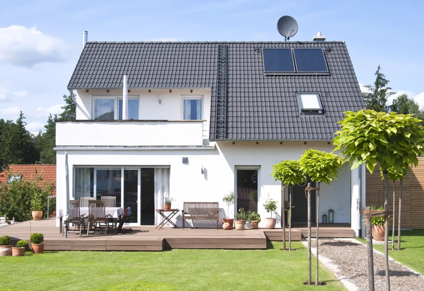 Modern detached house with two floors, balcony, terrace and pitched roof, as well as solar panels on the roof, surrounded by lawn.