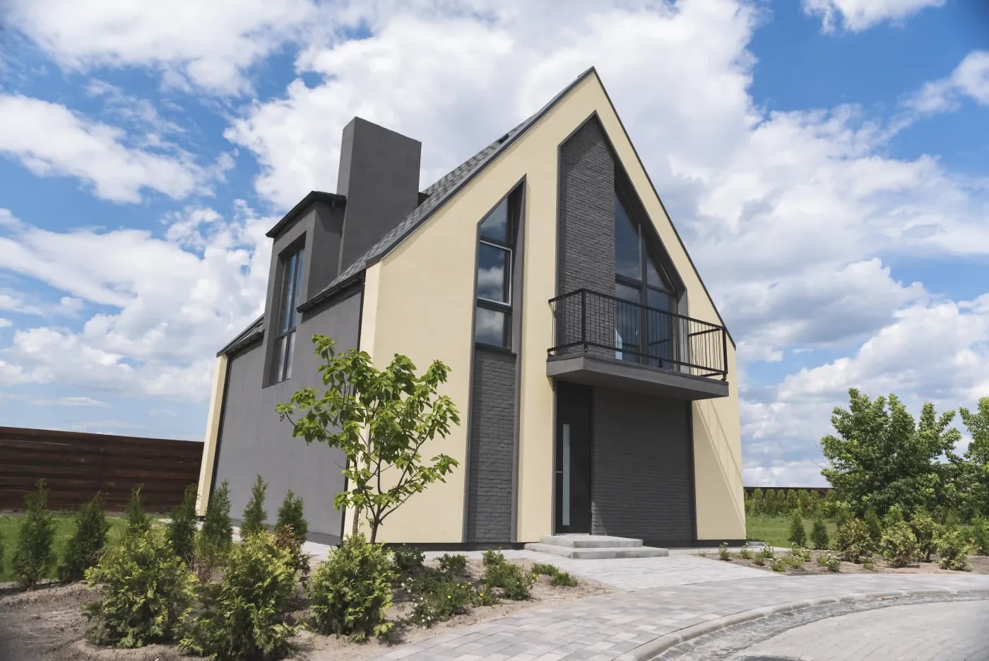 Eckansicht eines inzeln stehenden Einfamilienhaus mit Balkon an der Front, Satteldach mit Gaube an der Seite und frisch gepflanzter Begrünung im Vorgartenbereich.
