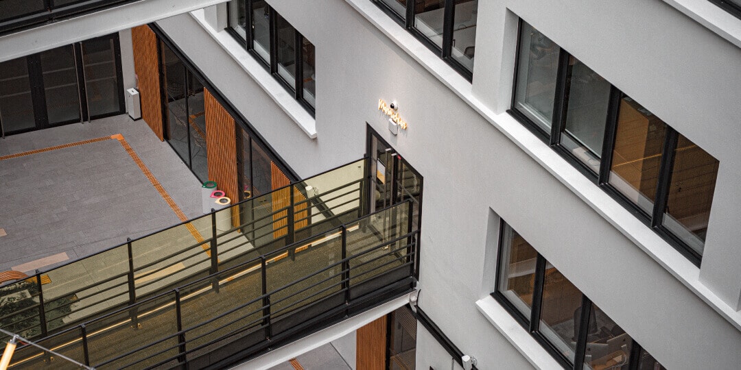 Bird's-eye view of the inner courtyard of a modern office building with a glazed walkway and wooden panels.
