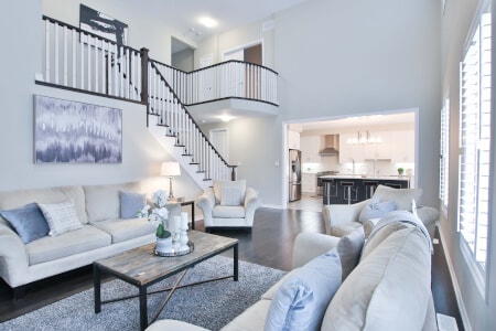 Staged living room with two white sofas, a rustic wooden coffee table and a staircase with black railings; view into a kitchen in the background.