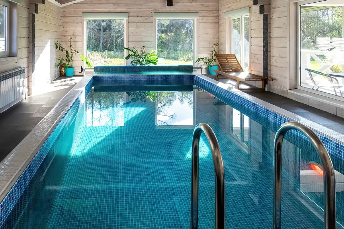 View from the short side of an indoor pool with an entry ladder in the foreground and large, wide panoramic windows all around