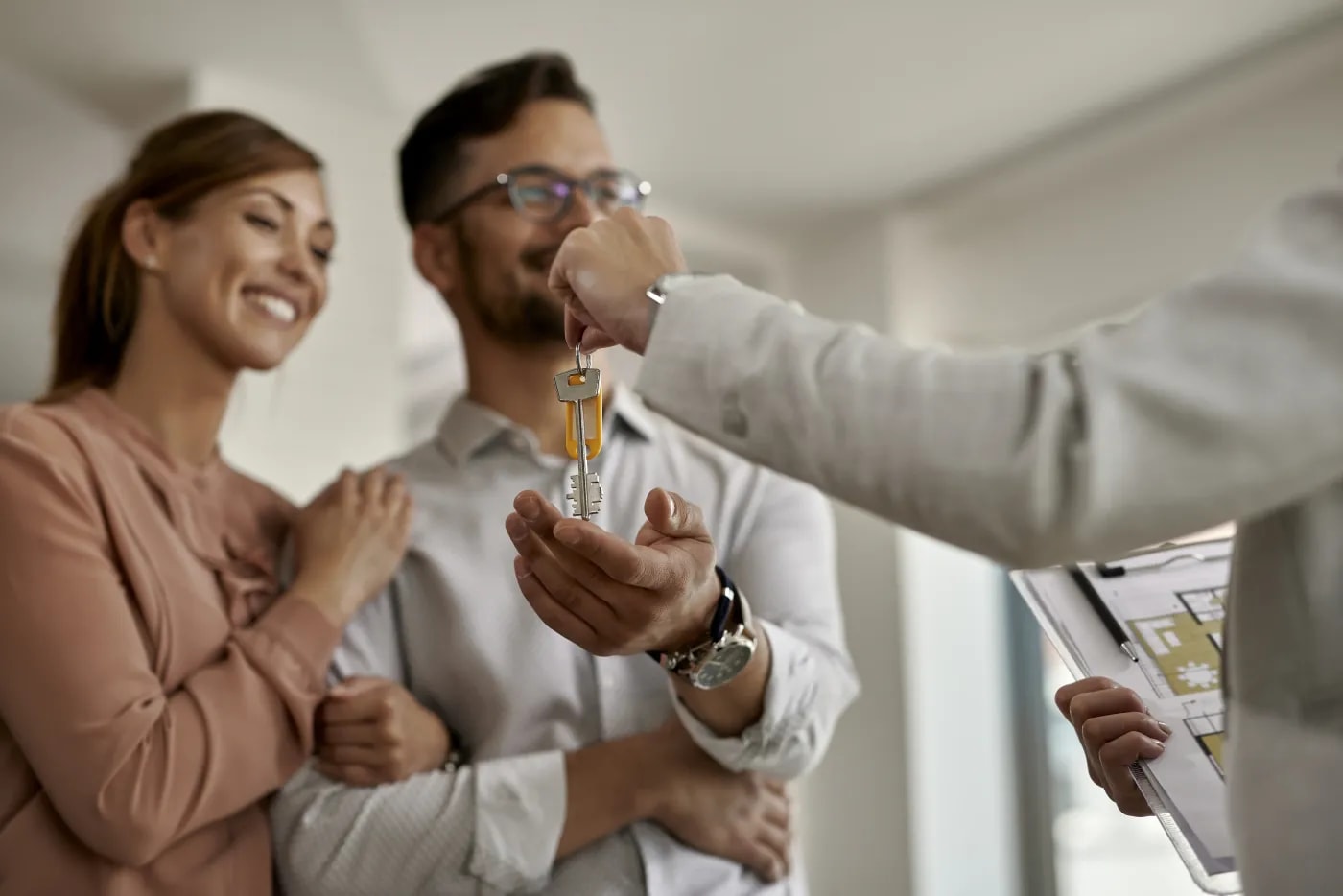 The female agent, clipboard in hand, hands the key to the apartment over to the happy couple.
