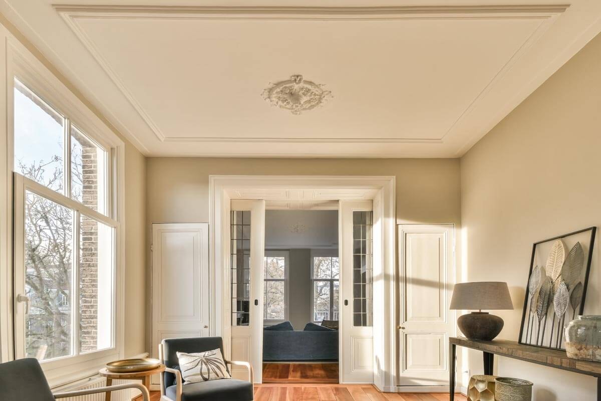 Heller Salon mit breiter Fensterfront, Stuckdecke und Durchgang mit Schiebetür in den hinteren Teil des Raumes.