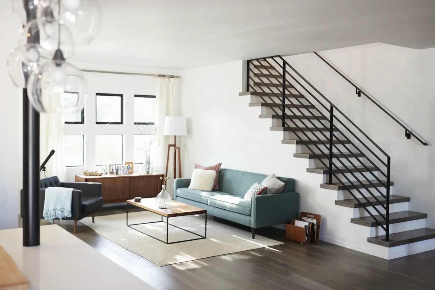 Blick aus der Zimmerecke in ein Wohnzimmer mit modernem Sitzbereich vor der Seitenwand mit kleinen Fenstern und einer Treppe ins Obergeschoss rechts an der Wand.