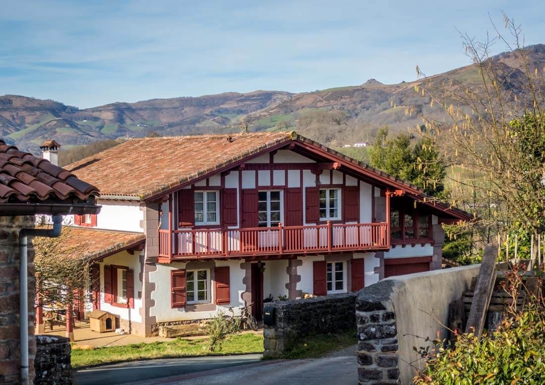 A typical mountain accommodation hut in half-timbered style with a shallow pitched roof, balcony and wooden shutters set against a late-summer mountain landscape.