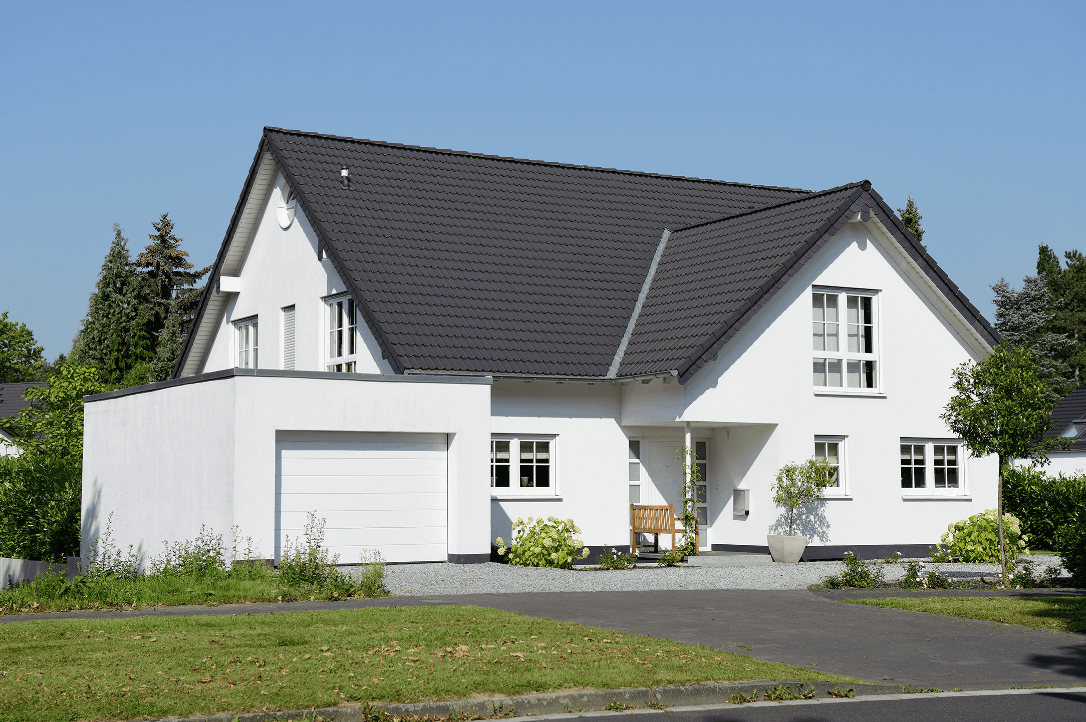 Exterior view of a multi-story, modern L-shaped single-family house with a garage and a dark gable roof