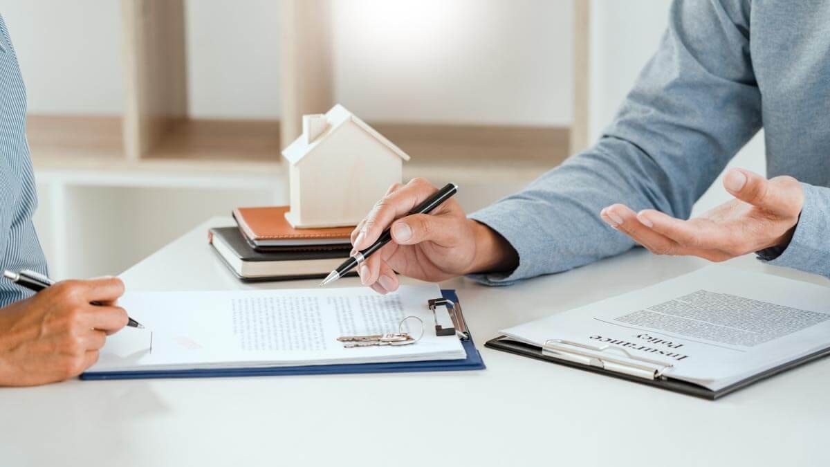 Close-up of a broker's and a client's hands at a table, going through contract documents together.