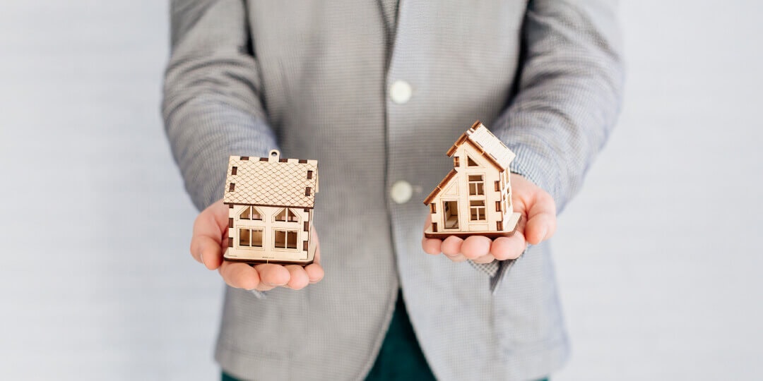 Two small wooden model houses lying in the open palms of a person.