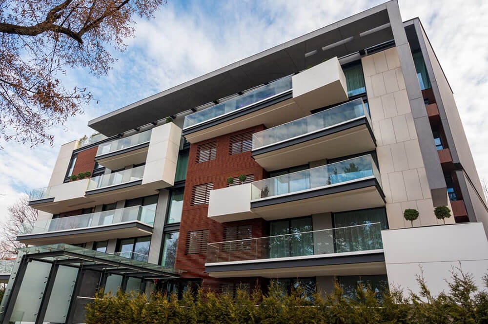 Modernes Mehrfamilienhaus mit assymmetrischer Fassade und Elementen aus Glas und Beton, sowie Balkonen mit Glasplatten-Umrandung.