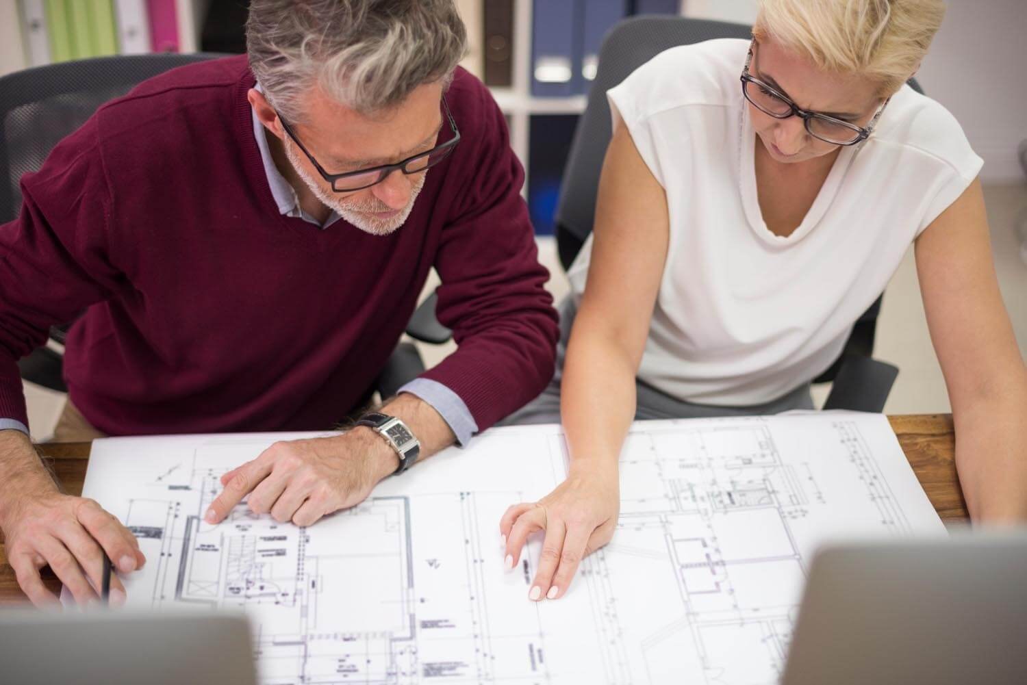 A man and a woman lean in to discuss a floor plan showing two levels of a building
