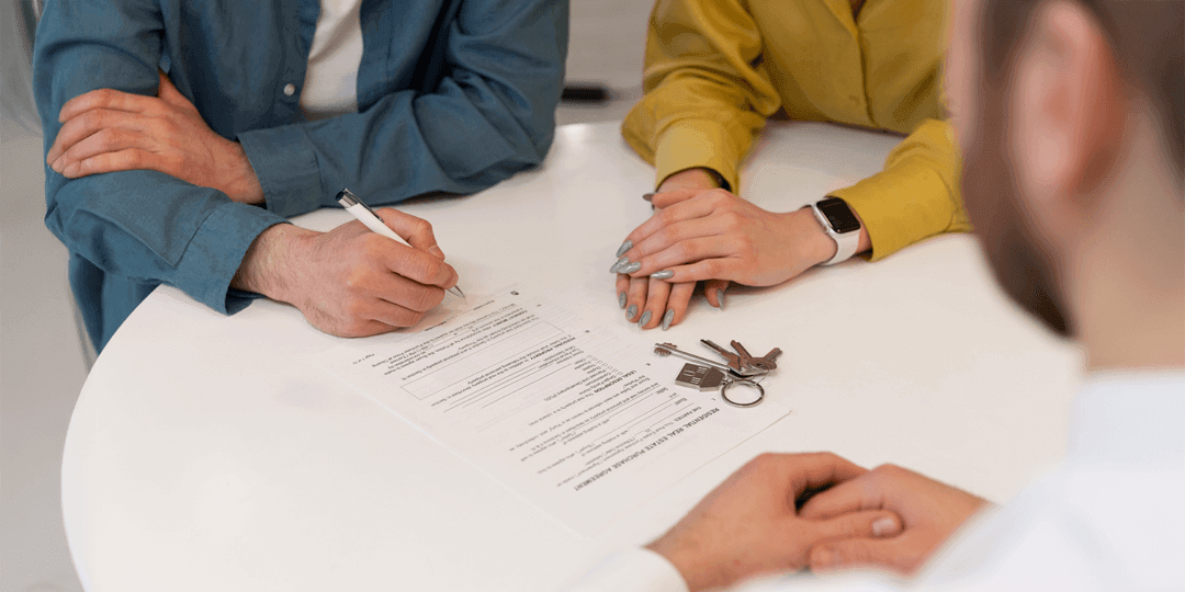 View over the shoulder of a real estate agent of a couple sitting at a table signing a contract