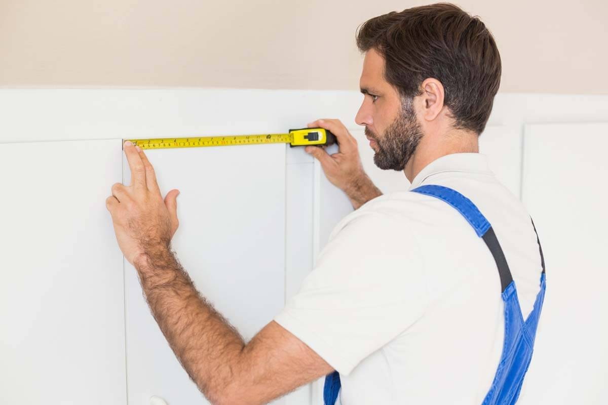 Skilled worker taking measurements on a white paneled wall surface