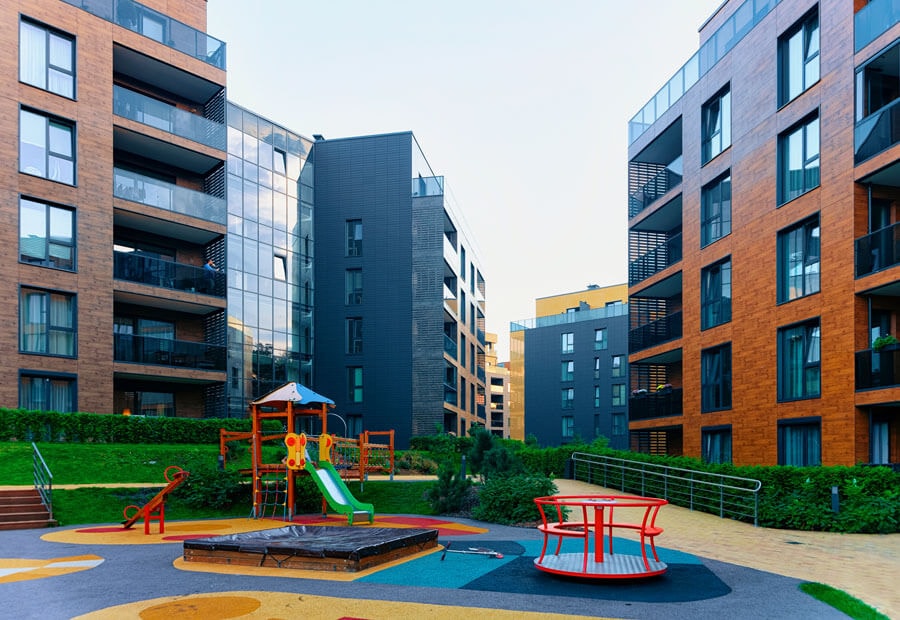 Realistische 3-d Konzeptart einer modernen Wohnsiedlung aus mehreren mehrgeschossigen Mehrfamilienhäusern, die sich um einen zentralen Kinderspielplatz mit Ziergrünanlagen gruppieren.
