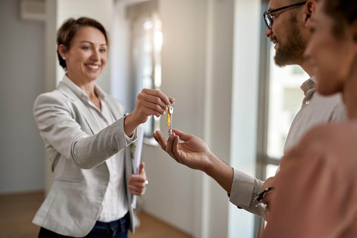 A real estate agent hands an apartment key to a smiling couple