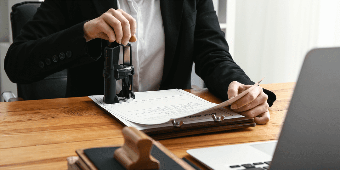 Close-up of a real estate agent sitting at a desk, stamping several documents on a clipboard with a large stamp