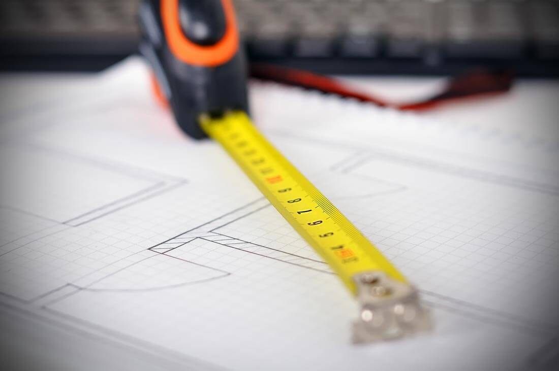 Close-up detail shot of an extended measuring tape lying on a floor plan.