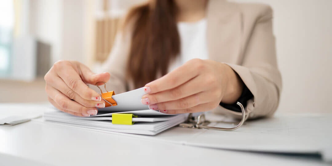 Close-up of hands sorting documents in a ring binder with coloured binder clips.
