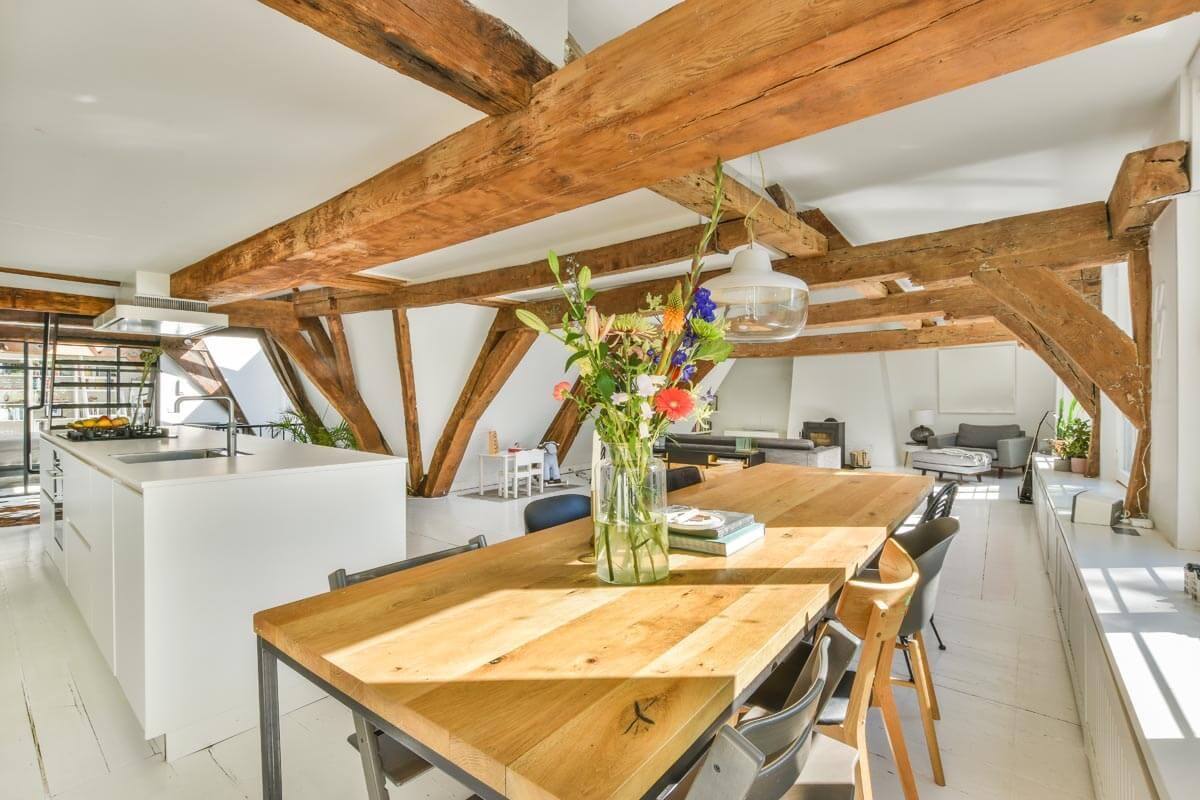 L-förmiger Raum unter dem Dach mit partiellen Schrägen und niedriger Decke und eng gestellten Möbeln, wie einer Sitzgruppe, Sideboards und im Hintergrund Polstermöbel.