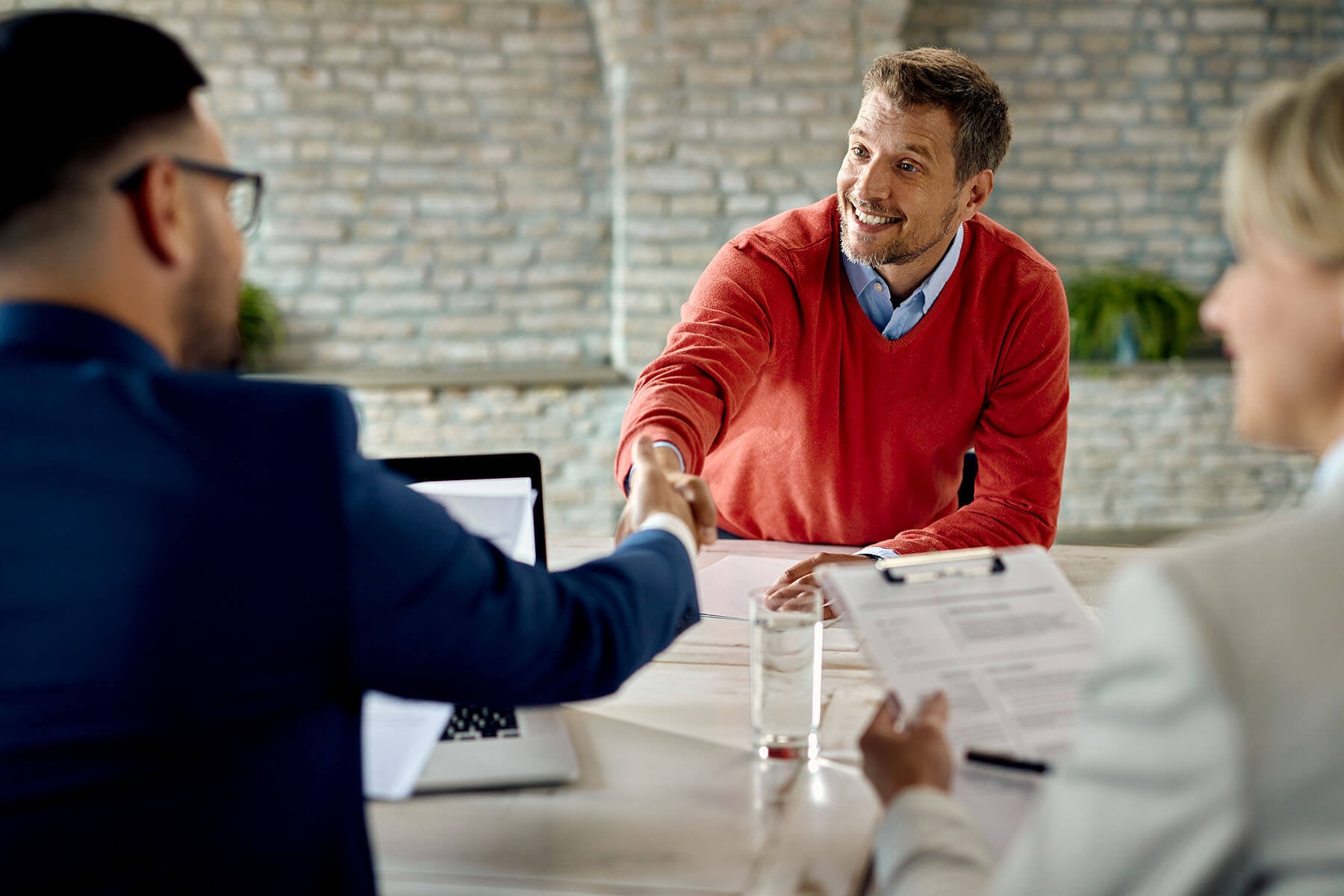 A tax advisor at a table with a colleague shakes a client's hand across the table