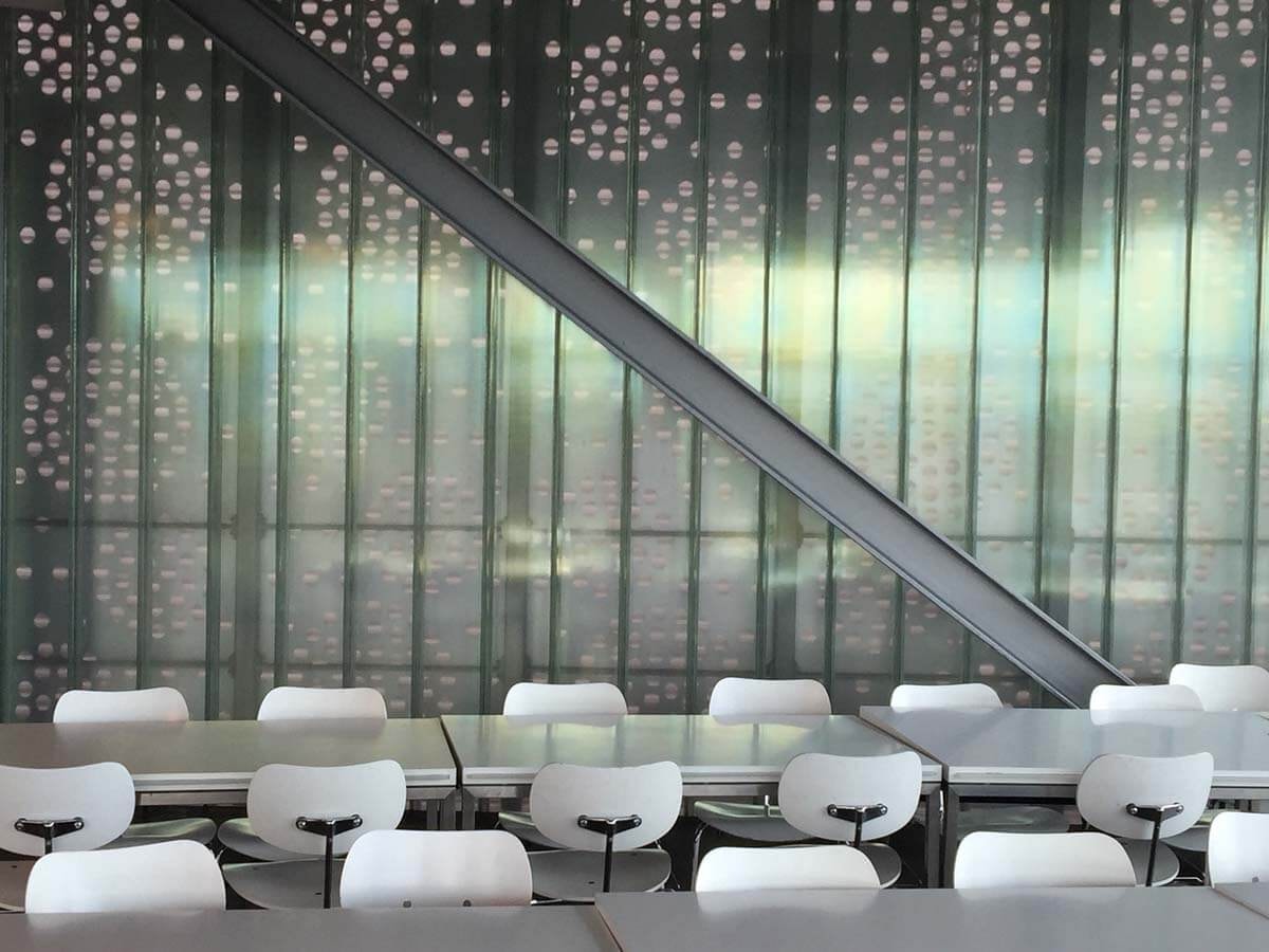 Side view of two rows of tables with white chairs on both sides and a wall with an industrial workshop appearance in the background.