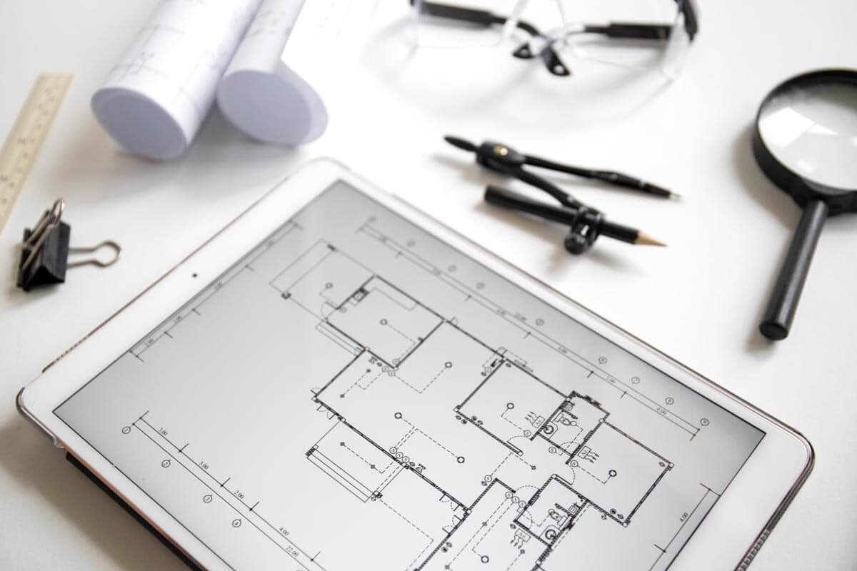 Tablet displaying a floor plan on screen, surrounded by several drawing instruments for sketching a floor plan by hand.