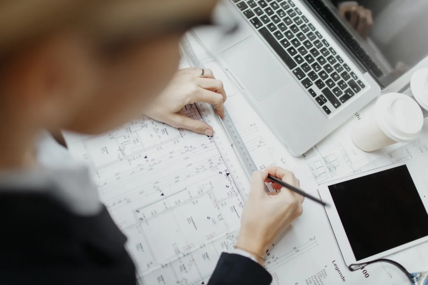 Over-the-shoulder view of a graphic designer drawing a line on a floor plan with a pencil and ruler.