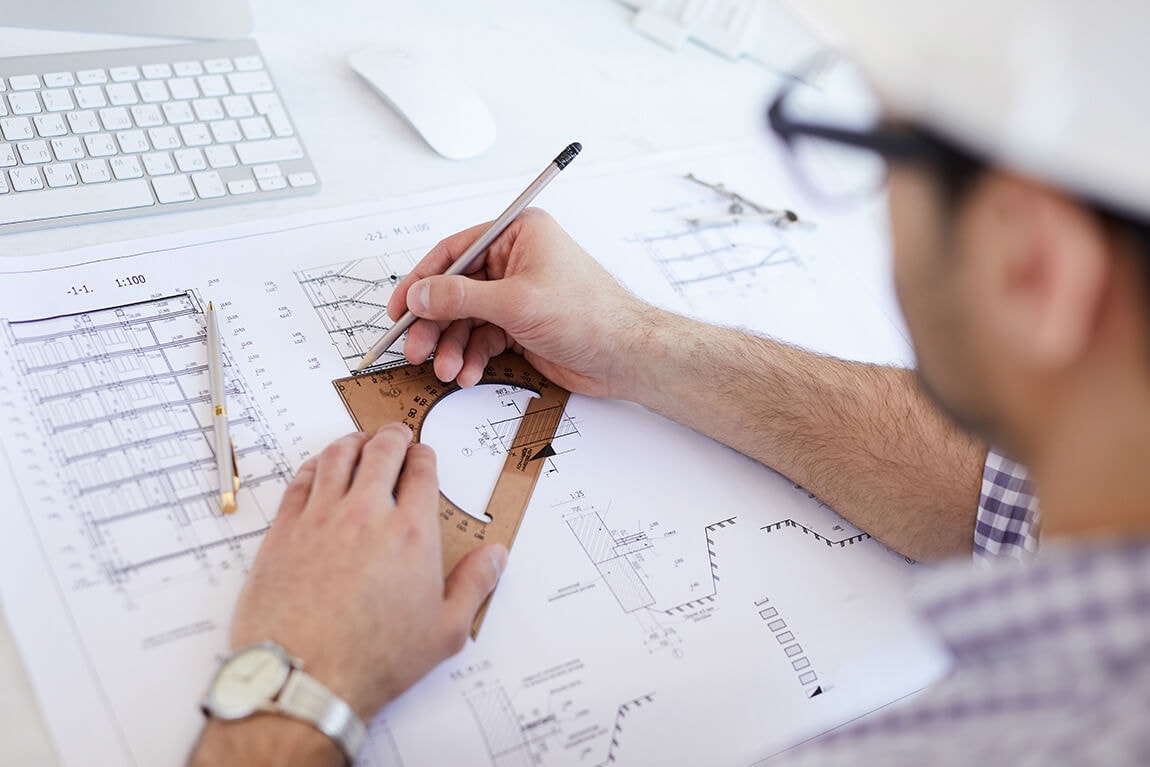 Over-the-shoulder view of an architect refining a line with a wooden set square.