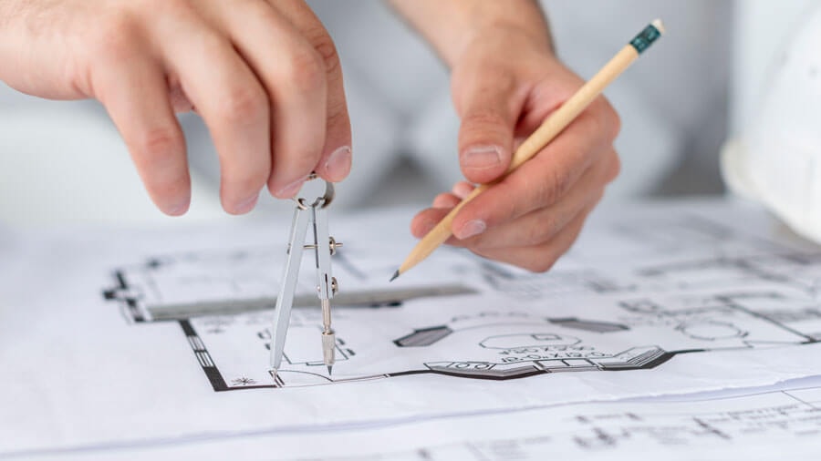 Close-up of two hands holding a compass and a pencil over a floor plan.