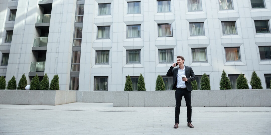 Man in a suit on the phone in front of a modern building with a distinctive geometric window facade.