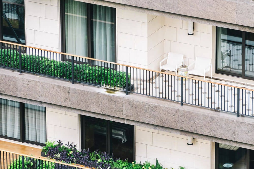 Detailed view of a balcony on a townhouse with light-colored brickwork, light greenery, and large windows