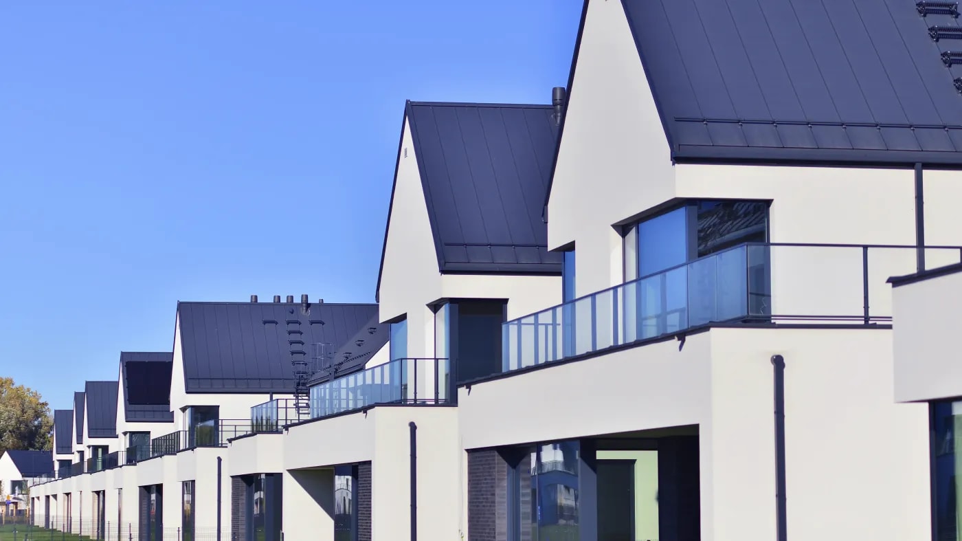 Modern terraced houses with light render and black roof tiles, balconies with glazed railings and a deep blue sky above.