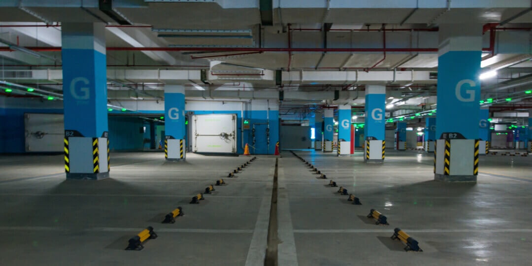 Empty underground car park with blue concrete columns, parking space markings and secured parking barriers on the floor.