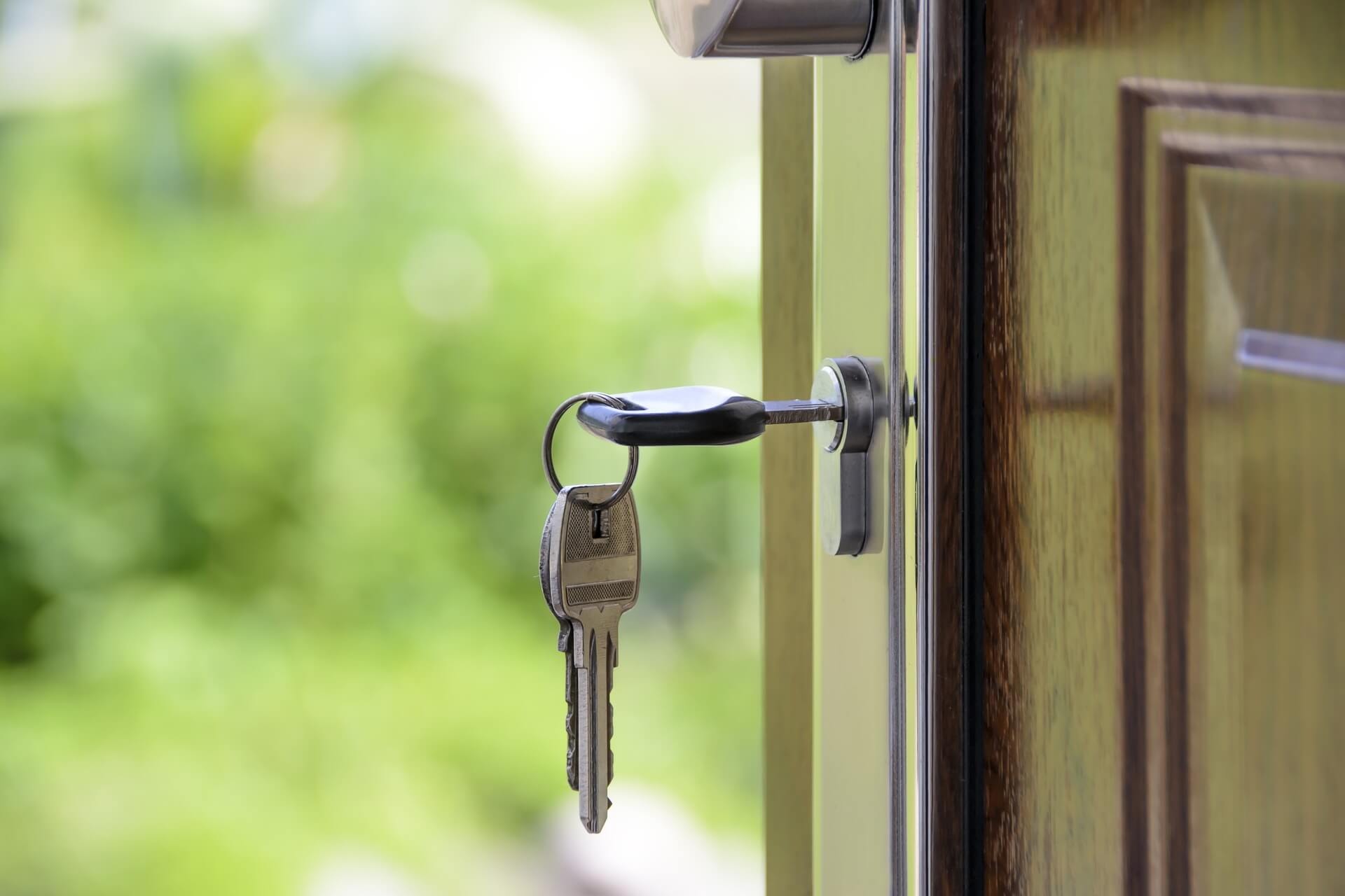 Close-up of a house key turned in the lock of a wooden door against a background of lush greenery.