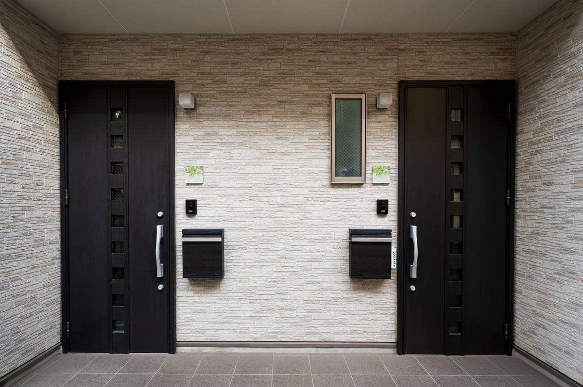 Photo of the side-by-side entrances of a semi-detached house with a light stone facade and dark brown front doors and letterboxes.