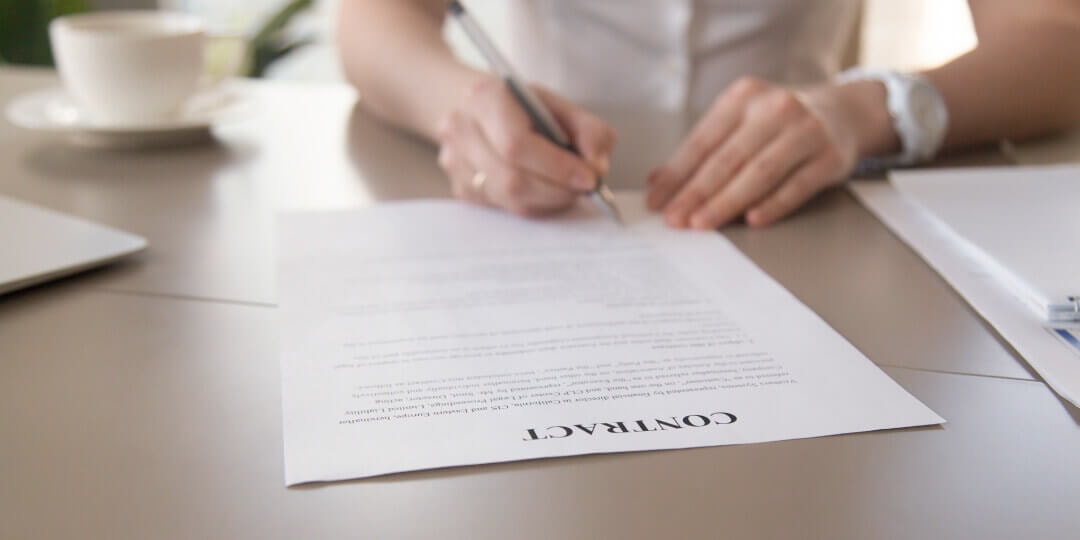 Woman's hands signing a contract on a desk, with a coffee cup beside it.