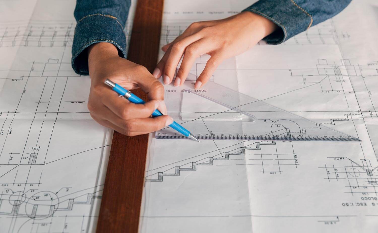 A hand with a pen marks a staircase on a floor plan using a ruler and a set square